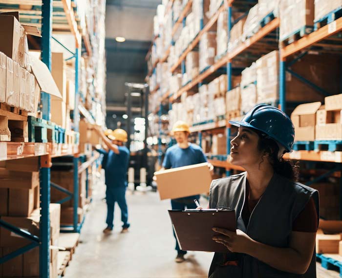 Busy warehouse scene with people in hardhats and high, stocked shelves.